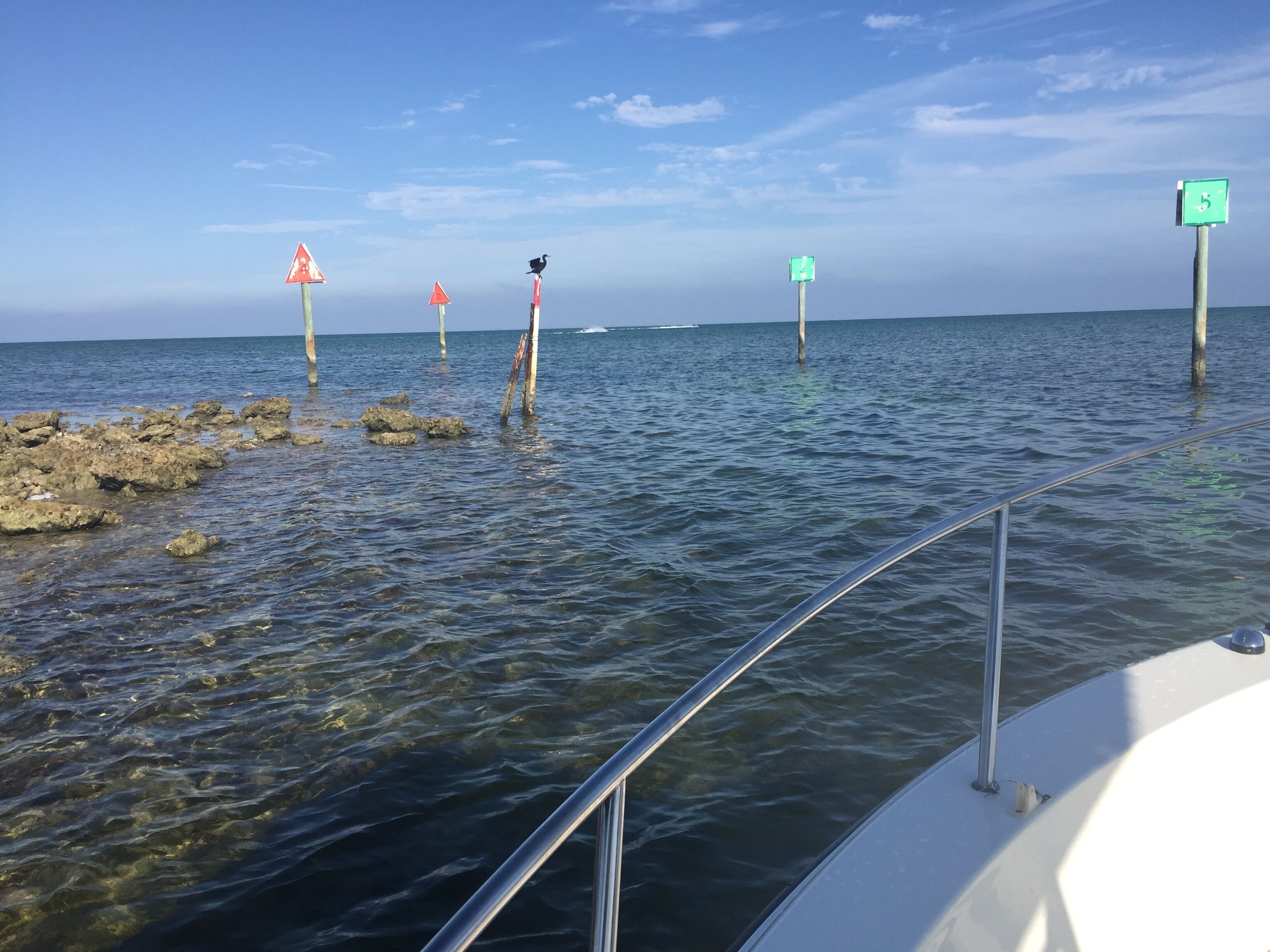 Ein Boot mit Metallgeländern und eine felsige Küstenlinie mit Warnschildern im Wasser.