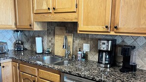 Una cocina con armarios de madera, encimera de granito, lavavajillas Bosch, cafetera y pileta de acero inoxidable.