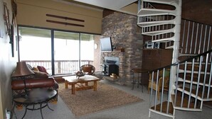 Una sala de estar acogedora con chimenea, pared de piedra, televisor y una escalera de caracol.