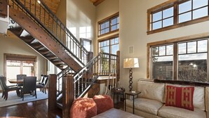 A spacious living room with a wooden staircase, a leather sofa, and a dining area with a table and chairs. - Incredible luxury townhome in downtown Whitefish! 1 block from all downtown shops and restaurants (Whitefish)