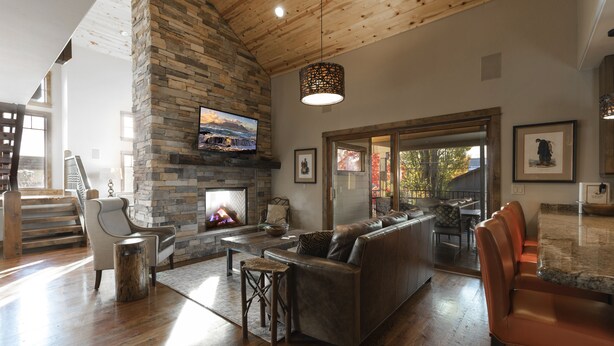 A spacious living room with a stone fireplace, a large flat-screen TV, a leather sofa, and a wooden ceiling. - Incredible luxury townhome in downtown Whitefish! 1 block from all downtown shops and restaurants (Whitefish)