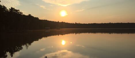 A calm lake at sunset with a boat docked on the left.