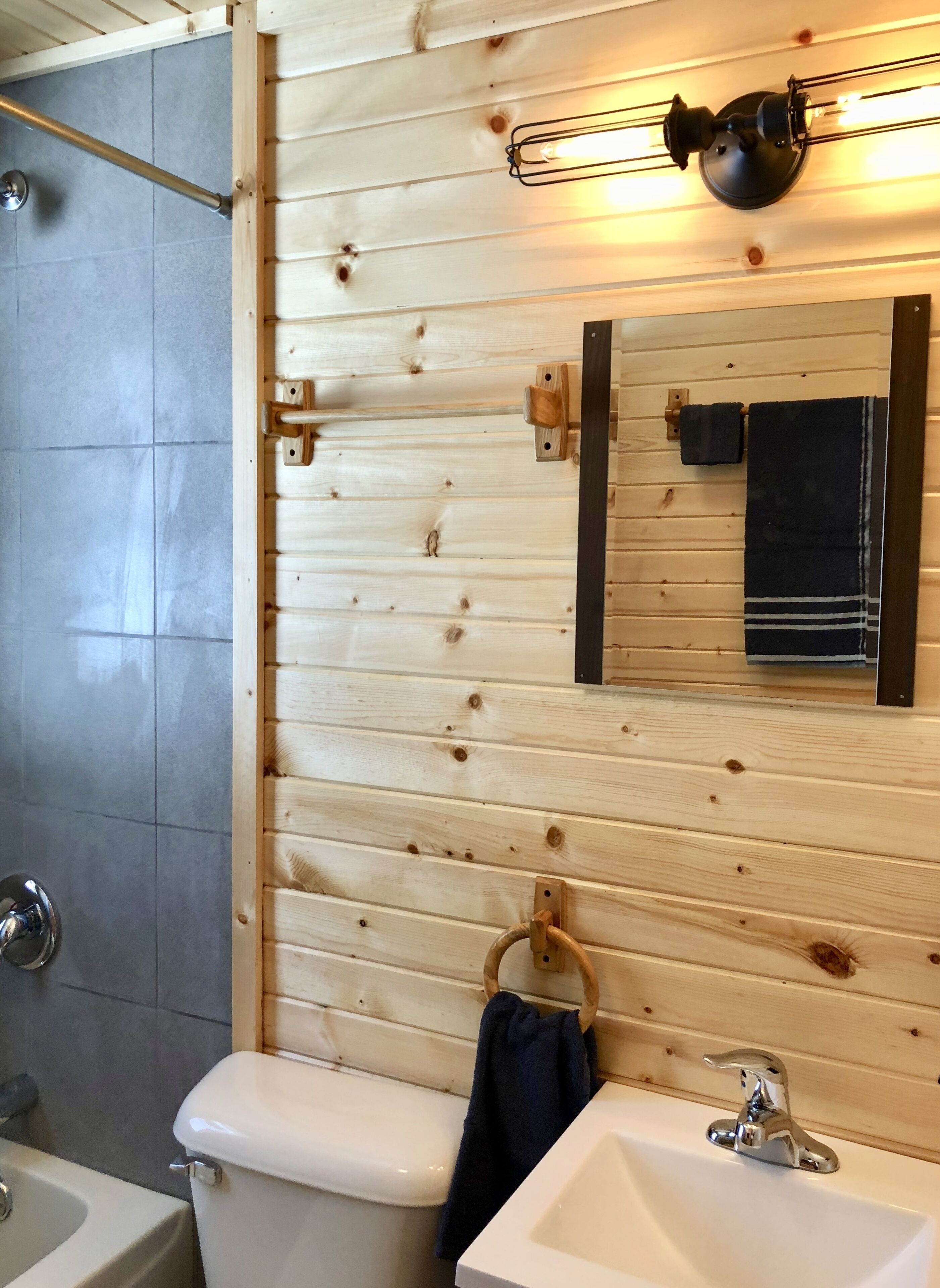 Een badkamer met een houten wand, een witte wastafel, een spiegel en een handdoekhouder.