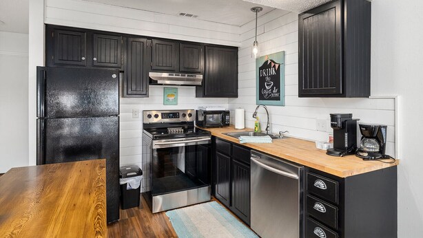 A modern kitchen with black cabinets, stainless steel appliances, and a wooden dining table. - Romantic getaway with a view; close to SDC and the Branson Strip (Branson West)