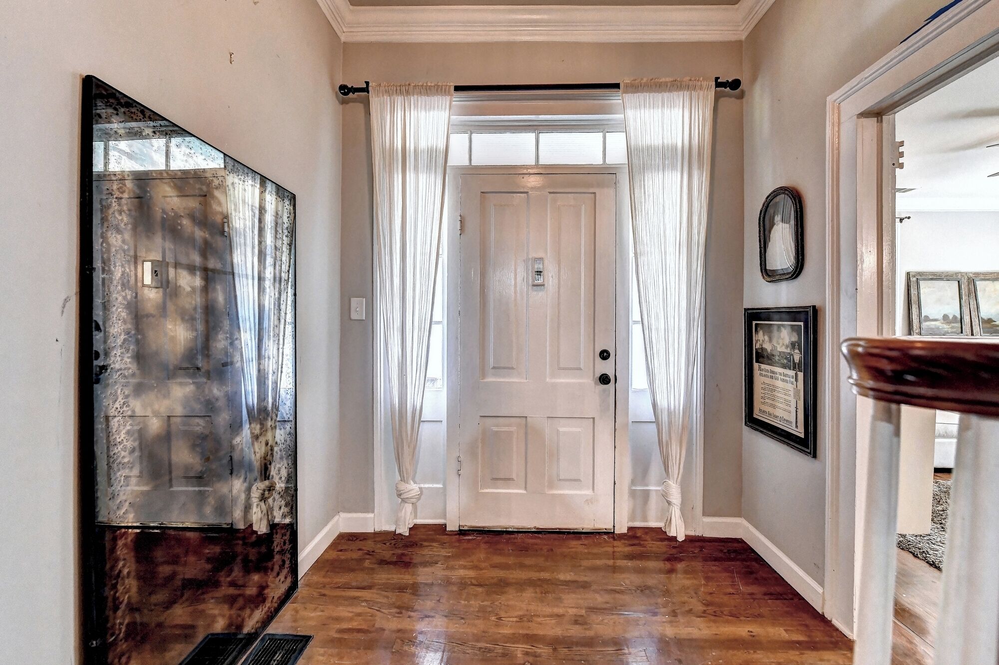 A hallway with a wooden floor, a white door with a window, and a mirror on the wall.