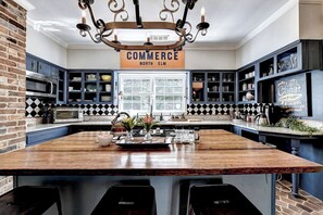 Una cocina con una isla central, armarios azules, una pared de ladrillo y un letrero que dice "COMMERCE NORTH ELM".