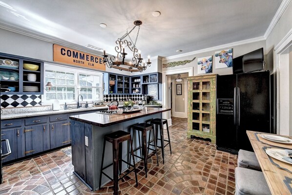 Una cocina con una isla central, taburetes de bar, un refrigerador negro y un letrero sobre la isla.