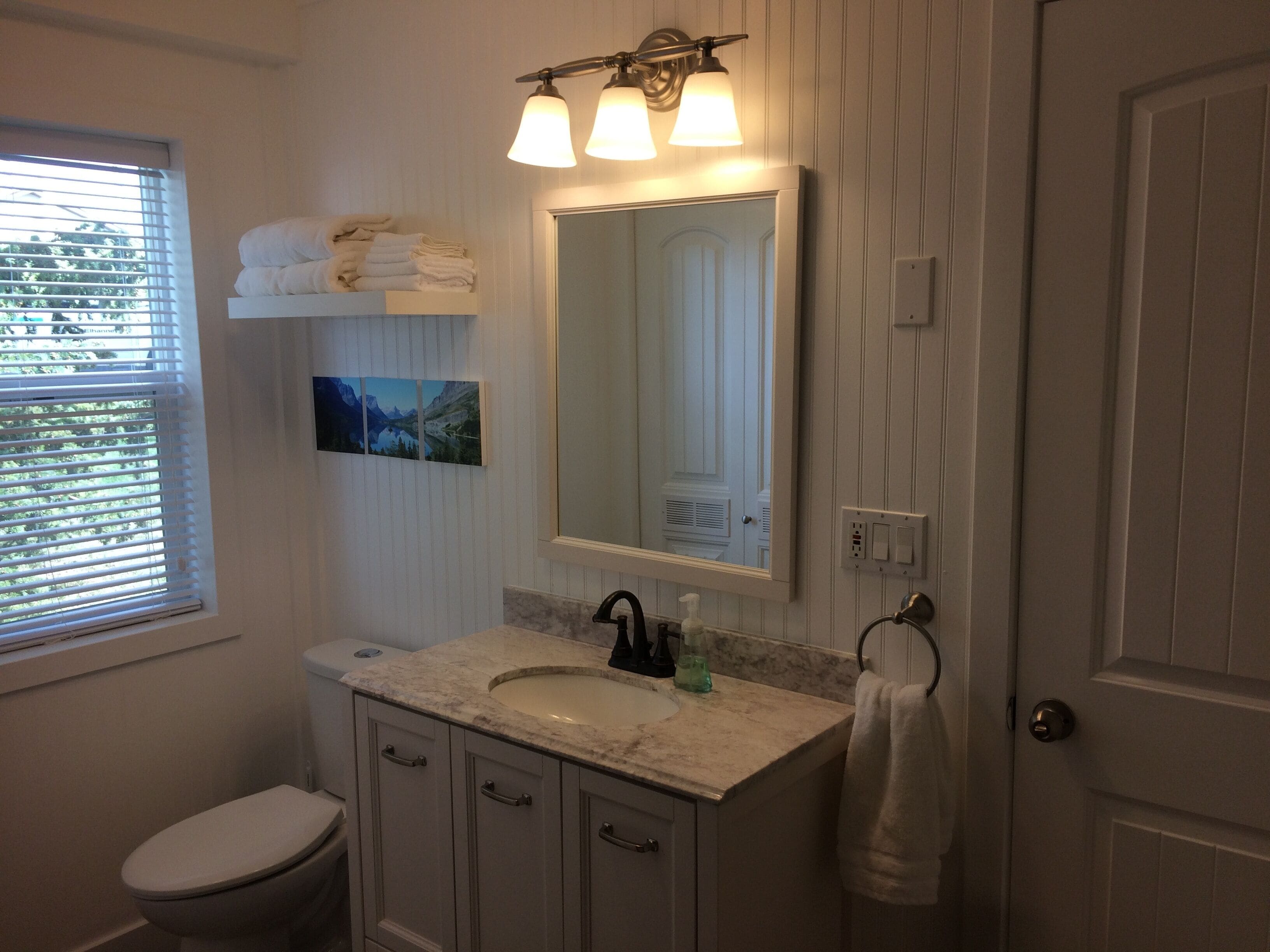 A bathroom with a toilet, sink, vanity, and a large mirror.