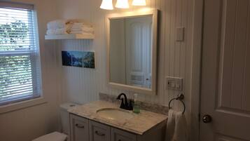 A bathroom with a toilet, sink, vanity, and a large mirror.