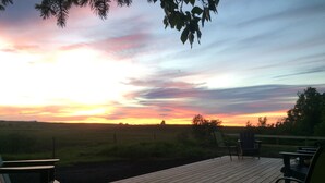En træterrasse med stole og borde, med udsigt over et mark ved solnedgang.