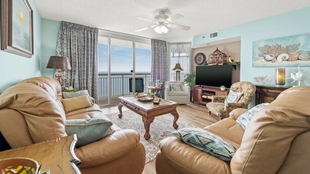 A living room with leather sofas, a coffee table, a TV, and a balcony with curtains. - Upscale Refined Unit, Oceanfront Water Amenities | Crescent Shores - N 1304 (North Myrtle Beach)