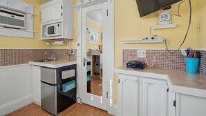 Cocina compacta con armarios blancos, microondas, refrigerador, lavabo y un televisor montado en la pared.