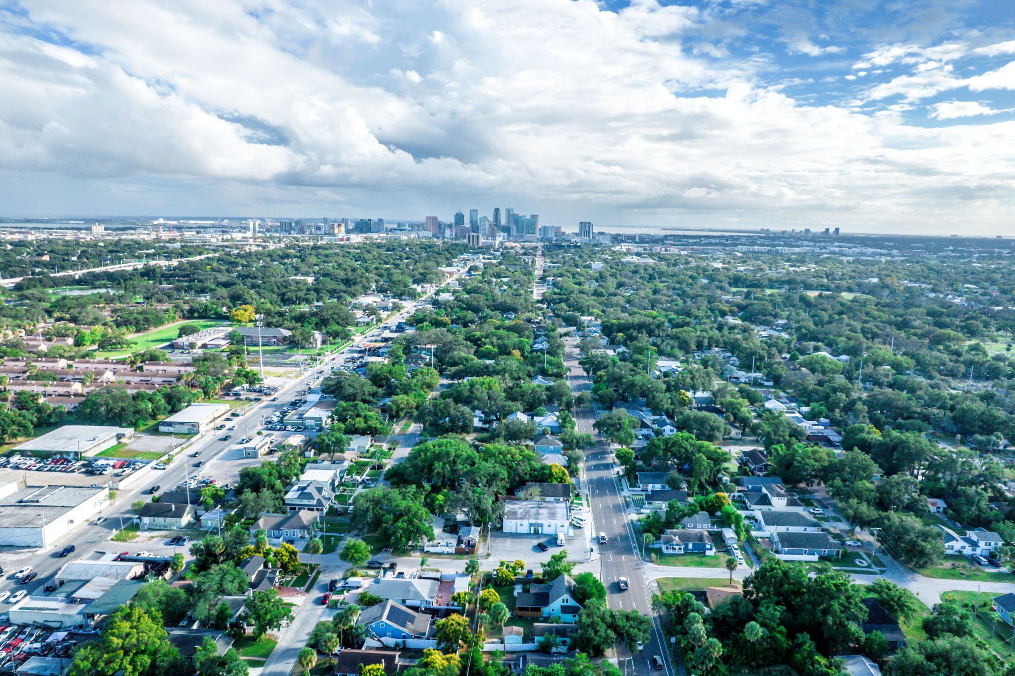 An aerial view of a residential area with houses, streets, and a distant city skyline.