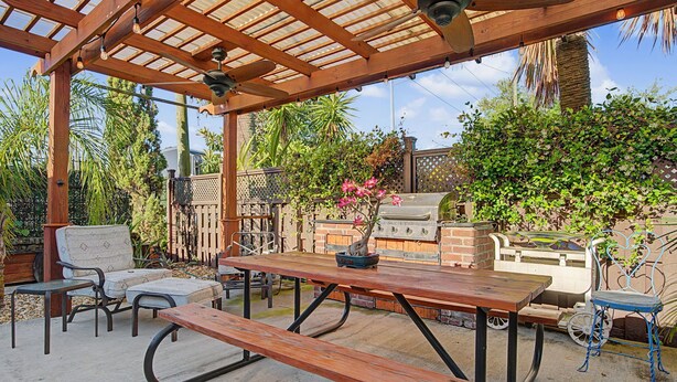 Un patio al aire libre con una mesa de madera, bancos y una parrilla.