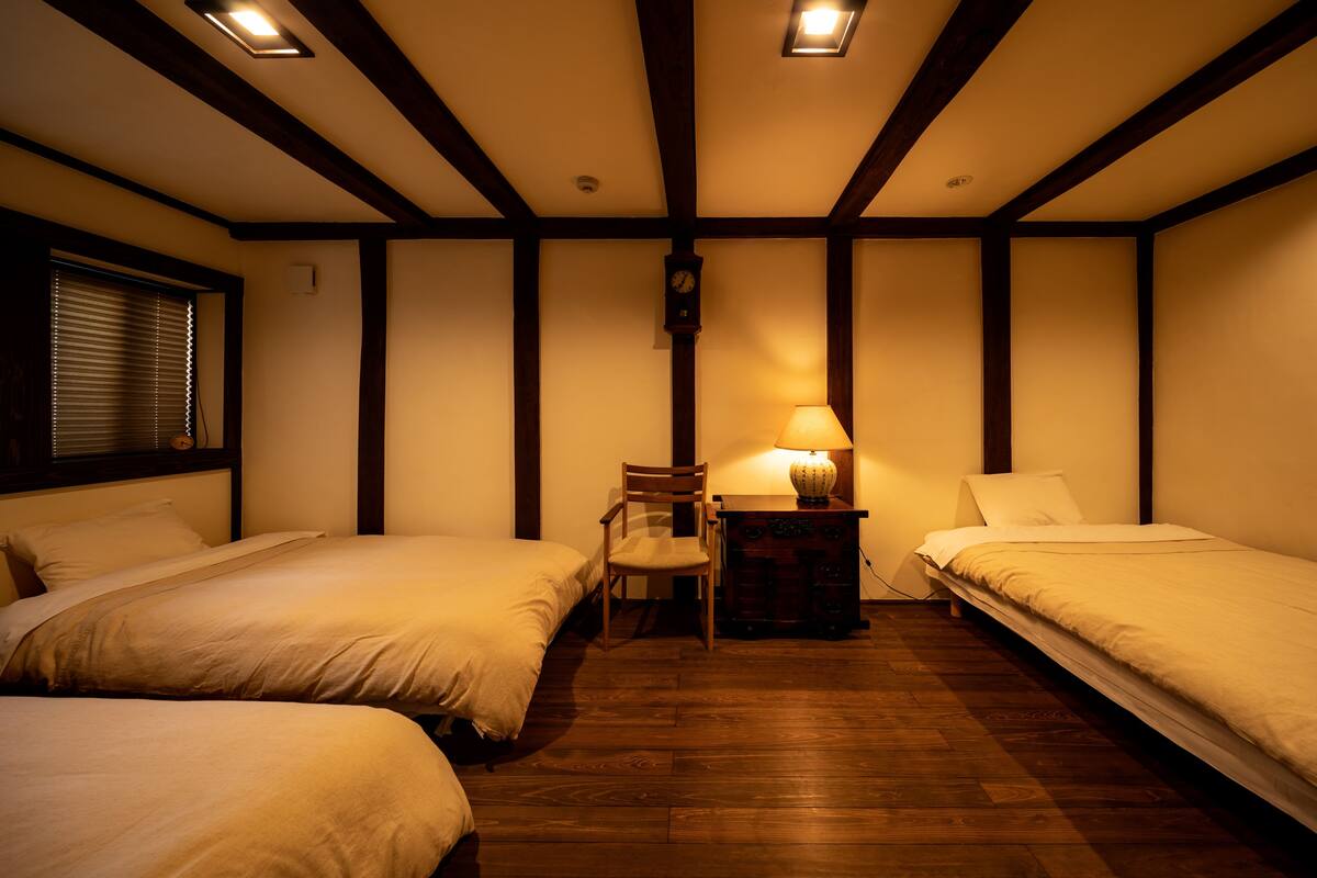 Habitació amb dos llits, una cadira, una tauleta de nit amb una làmpada i un rellotge de paret.