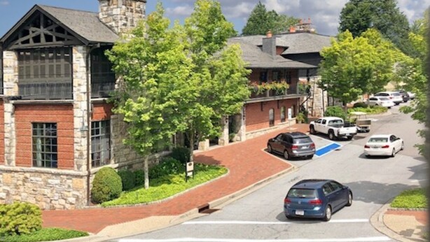 Une vue de rue avec une rangée de maisons en briques, un panneau bleu indiquant une place de stationnement réservée aux personnes handicapées, et des voitures garées le long de la route.