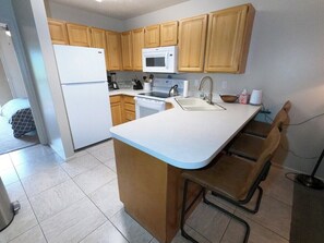 Une cuisine avec des meubles en bois, un réfrigérateur blanc, un four à micro-ondes, un évier et un tabouret de bar.
