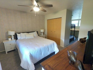 A bedroom with a bed, nightstands, a desk, a fish sculpture, and a ceiling fan.