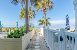 A pathway leading to a beach with palm trees and umbrellas. - NEW! Indian Rocks Beach Cottage Steps from Ocean! (Indian Rocks Beach)