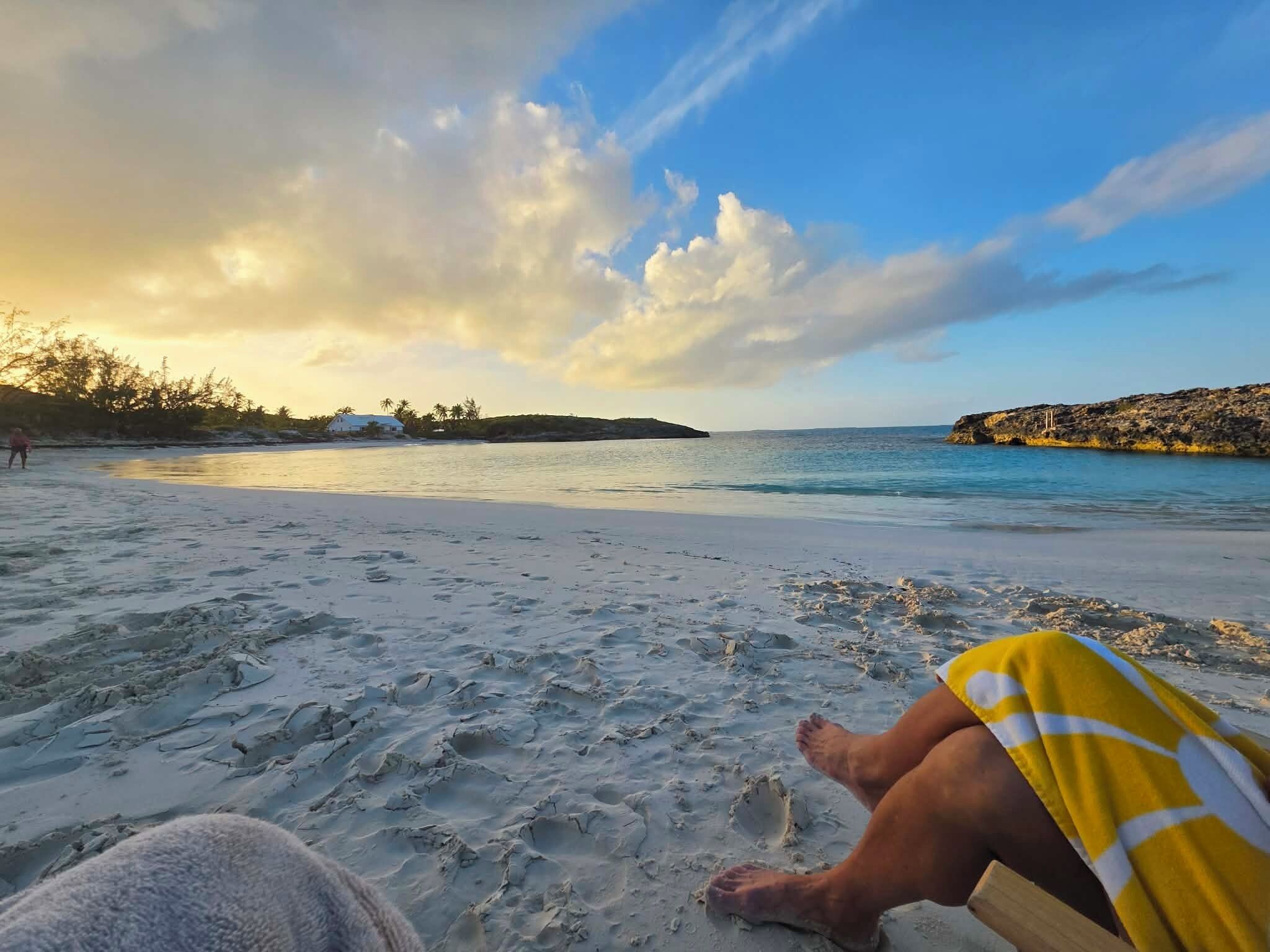 A beach with a person sitting on a beach chair, a sandy shore, and a calm sea.