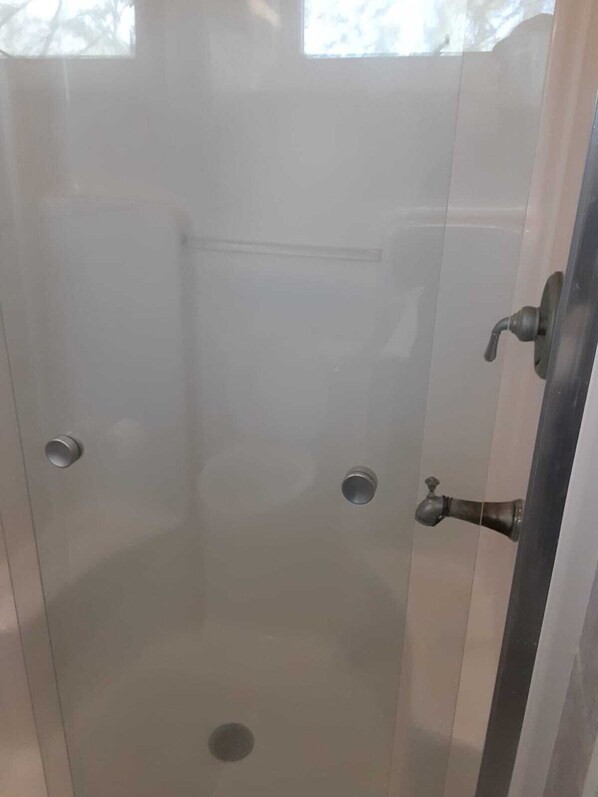 A glass-enclosed shower stall with a single faucet and a drain.