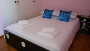 Una cama bien hecha con ropa de cama y toallas blancas, un aparador con cajones y una pared con un pequeño cuadro.