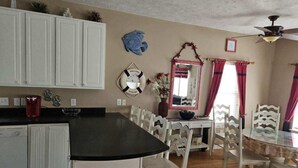 A kitchen with white cabinets, a black countertop, and a dining area with white chairs and a glass table. - Family‑Friendly Ocean‑View Home • 4BR/3BA • Steps to Beach • Sleeps 8‑10 (Myrtle Beach)
