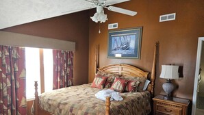 A bedroom with a wooden bed, a nightstand with a lamp, a framed picture on the wall, and a ceiling fan. - Family‑Friendly Ocean‑View Home • 4BR/3BA • Steps to Beach • Sleeps 8‑10 (Myrtle Beach)