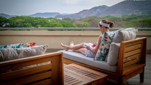 A person sitting on a wooden bench with a cushion, reading a book. - Condo w/ rooftop terrace & ocean views (Playa Hermosa,)