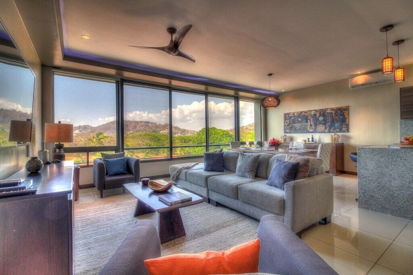 - Modern living room with panoramic mountain views - Floor-to-ceiling windows flood space with natural light - Relax in plush seating with flat-screen TV and sleek decor