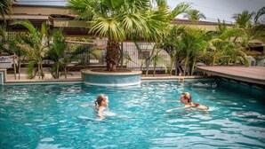 A swimming pool with two people in the water, surrounded by palm trees and a tiled deck. - Condo w/ rooftop terrace & ocean views (Playa Hermosa,)