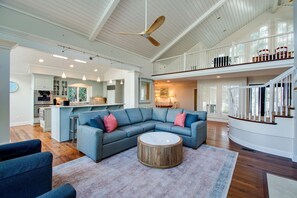 A spacious living area with a large sectional sofa, a round coffee table, and a ceiling fan.