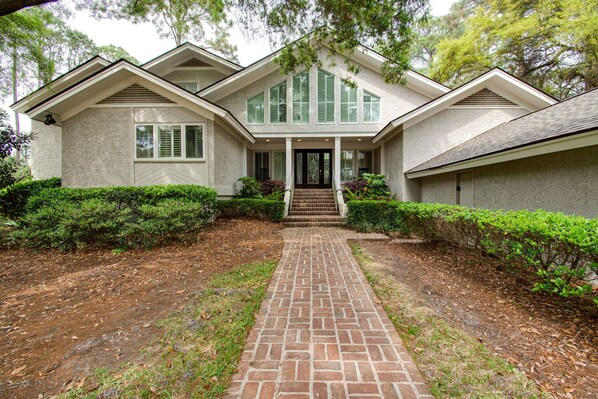 A two-story house with a brick pathway leading to the front door, surrounded by well-maintained hedges.