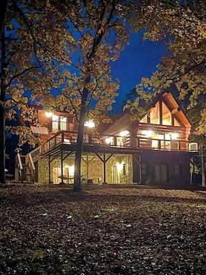 A two-story wooden house with a balcony, surrounded by trees.