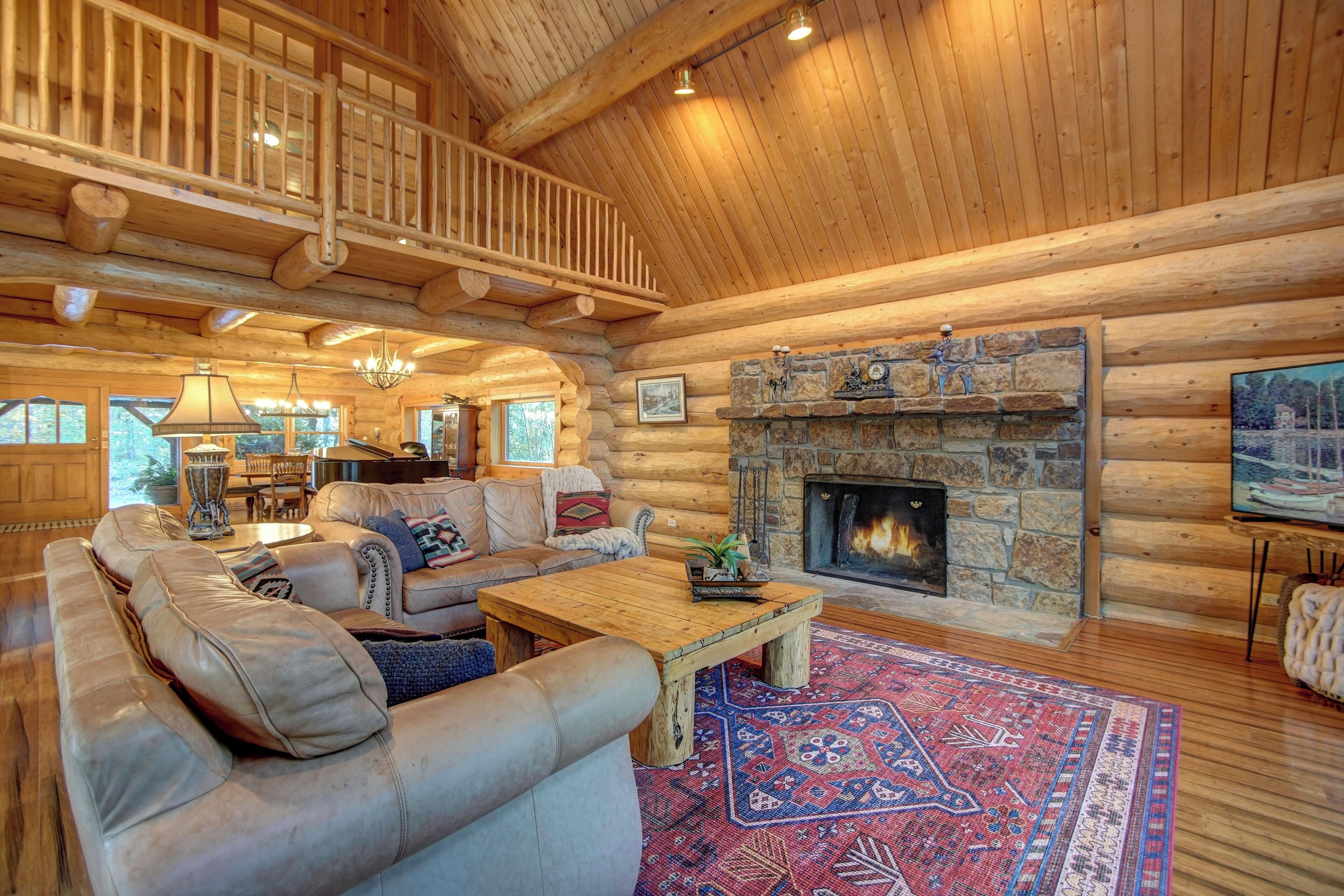 A log cabin interior with a stone fireplace, leather sofas, a wooden coffee table, and a staircase leading to an upper level.