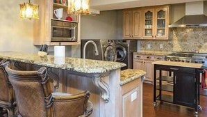 A kitchen with a central island, bar stools, a microwave, a stove, and a sink.