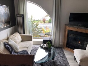 A living room with a sofa, coffee table, and fireplace. - Oceanside Honeymoon Suite (Qualicum Beach)