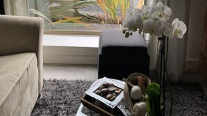 Quarto com vista para o mar, um sofá, uma mesinha com um recipiente de frutos secos e uma orquídea em vaso.