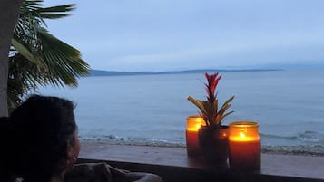 A person seated by a window overlooking a beach with candles on the windowsill.