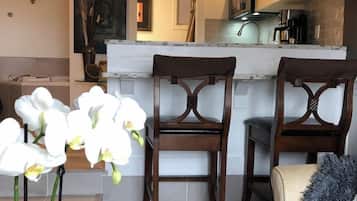 A modern kitchen with a white countertop, wooden chairs, and a decorative plant.
