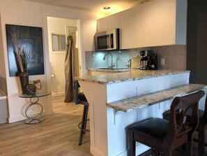 A compact kitchen with a microwave, coffee maker, and a small bar area. - Oceanside Honeymoon Suite (Qualicum Beach)