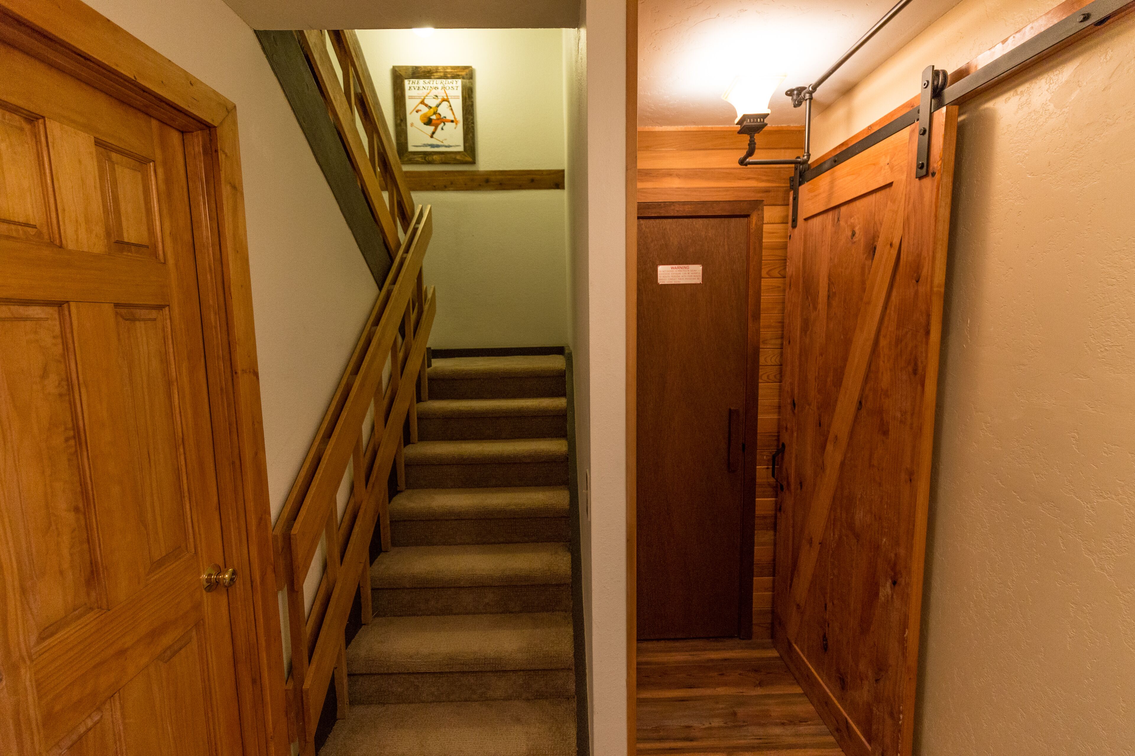 Un escalier en bois, doté d’une rampe, mène à une porte sur laquelle est apposé un panneau d’avertissement.