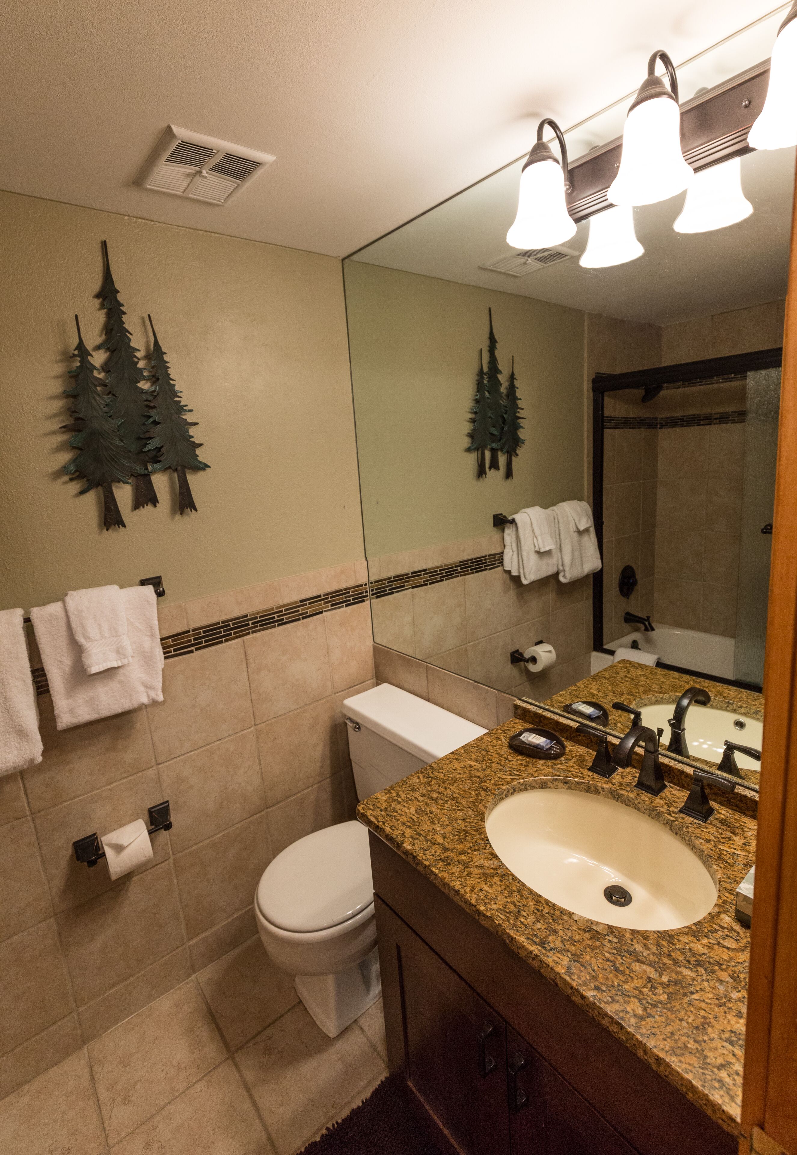 A bathroom with a toilet, sink, and mirror. There are towels hanging on the wall and a shower visible in the background.