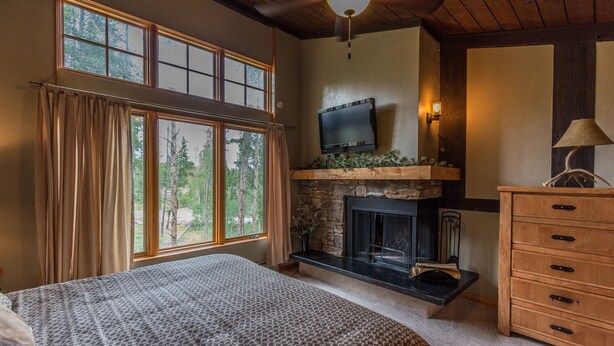 A bedroom with a large bed, a stone fireplace, a TV mounted above it, and a wooden dresser. - Ski or Ride, Hike Or Bike This Is Your Paradise! (Breckenridge)