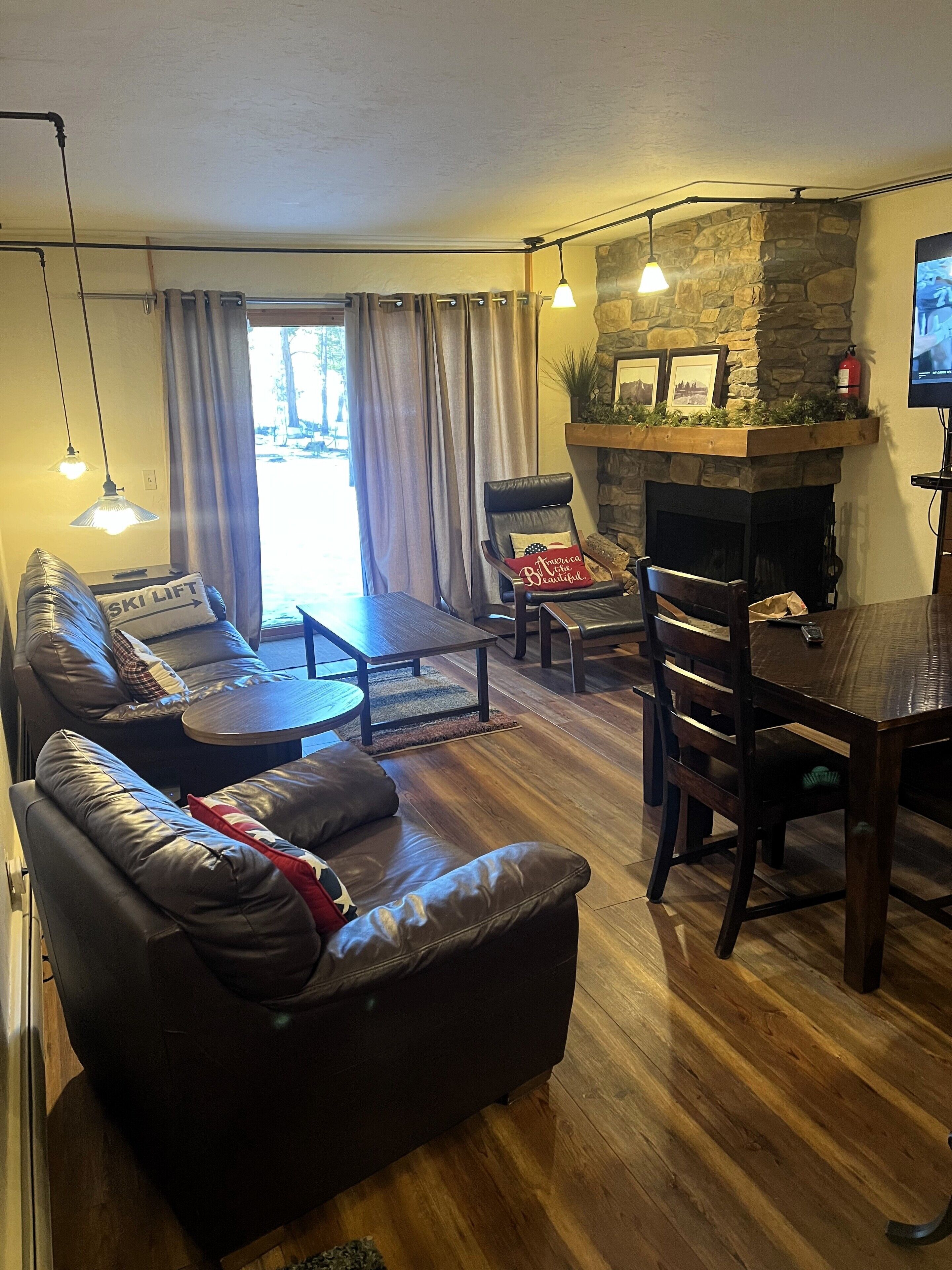 A cozy living room with a stone fireplace, leather sofas, and a dining table.