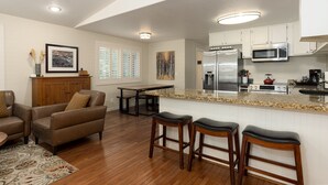 Una cocina con una isla central, taburetes de bar de madera, una mesa de comedor y un refrigerador.