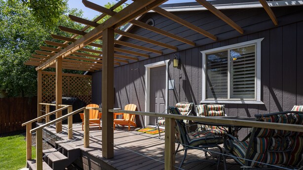 Una terraza con barandas de madera, mobiliario exterior y una zona cubierta con pérgola.