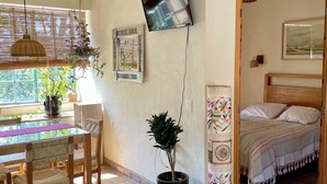 A cozy room with a bed, a dining table with chairs, a potted plant, and a TV mounted on the wall.