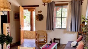 A cozy room with a wooden ceiling, a sofa, a chair, a table, and a window with curtains.