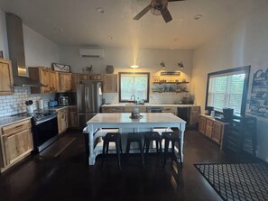 Una cocina moderna con una isla central, electrodomésticos de acero inoxidable, armarios de madera y un ventilador de techo.